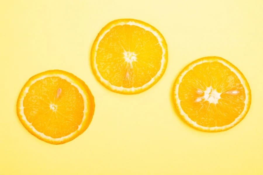Real orange slices with natural peel texture on a yellow surface.
